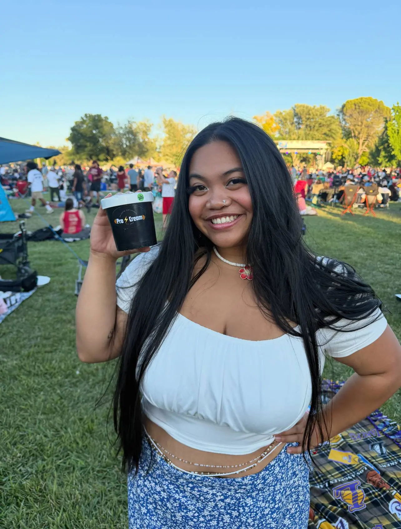 A smiling woman holding a drink at an outdoor event.