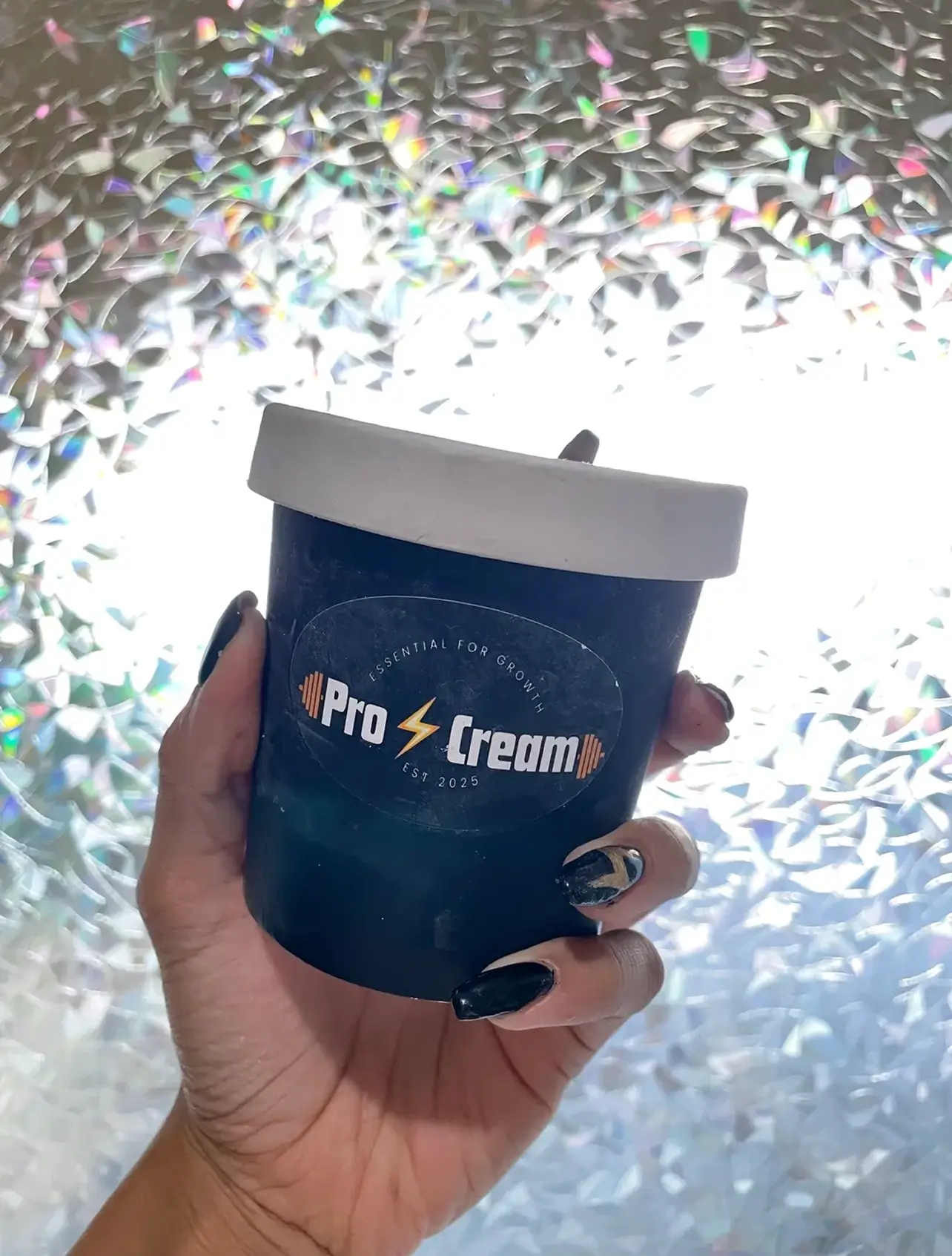 Hand holding a black jar labeled 'Pro Cream' with a white lid against a shiny background.